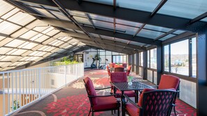 A covered outdoor seating area with a table and chairs, a patterned carpet, and large windows offering a view of the outdoors. - River Bend Inn (Pigeon Forge)