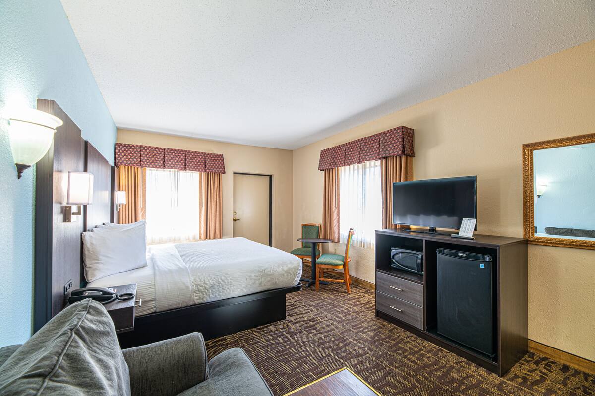 A hotel room with a bed, a desk with a television, a refrigerator, and a chair.