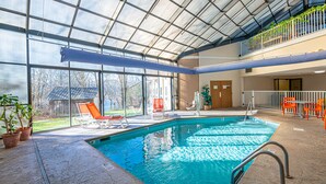 An indoor swimming pool with clear glass walls, a metal roof, and a view of the outside. - River Bend Inn (Pigeon Forge)