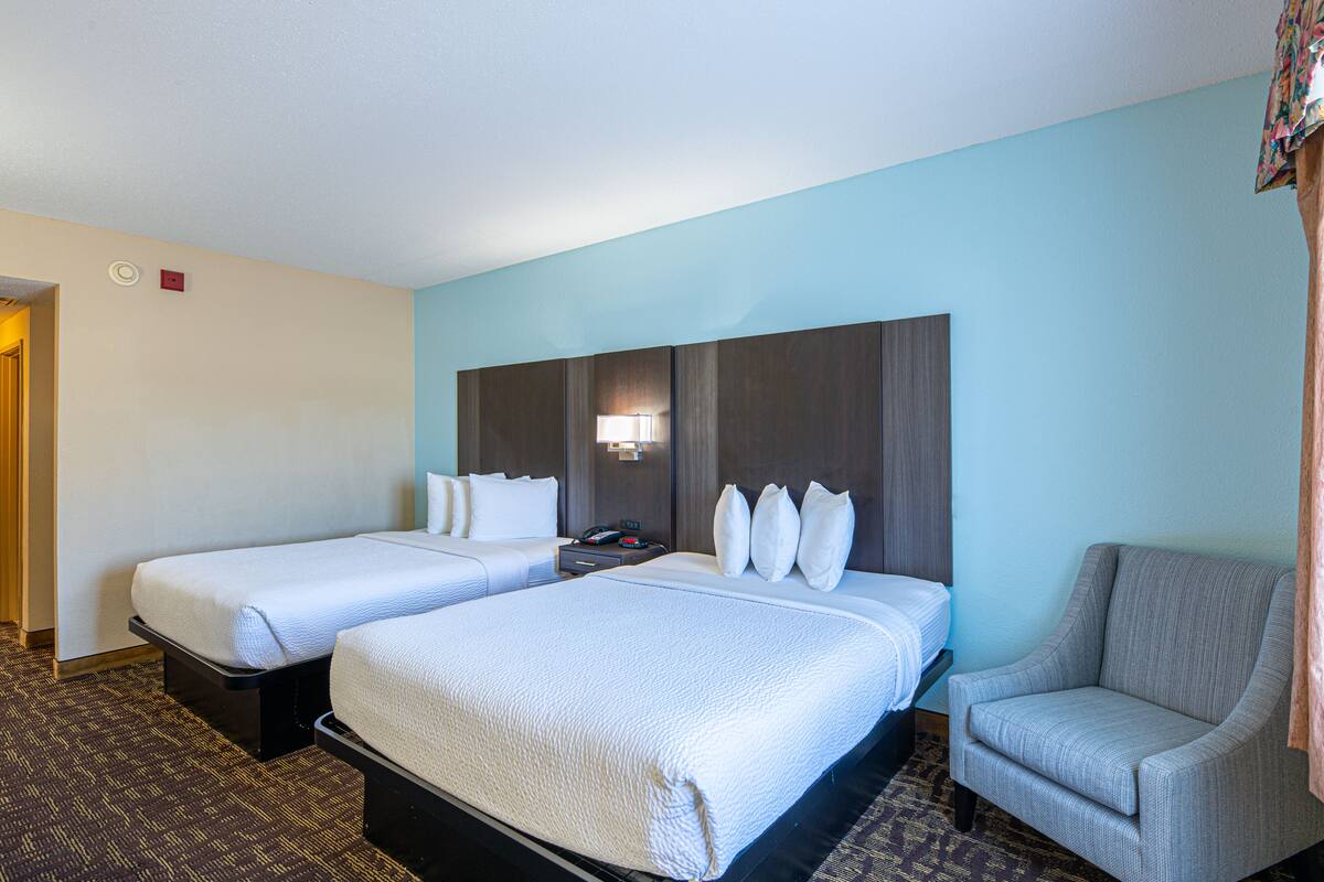 A hotel room with two beds, a chair, and a nightstand with a lamp.