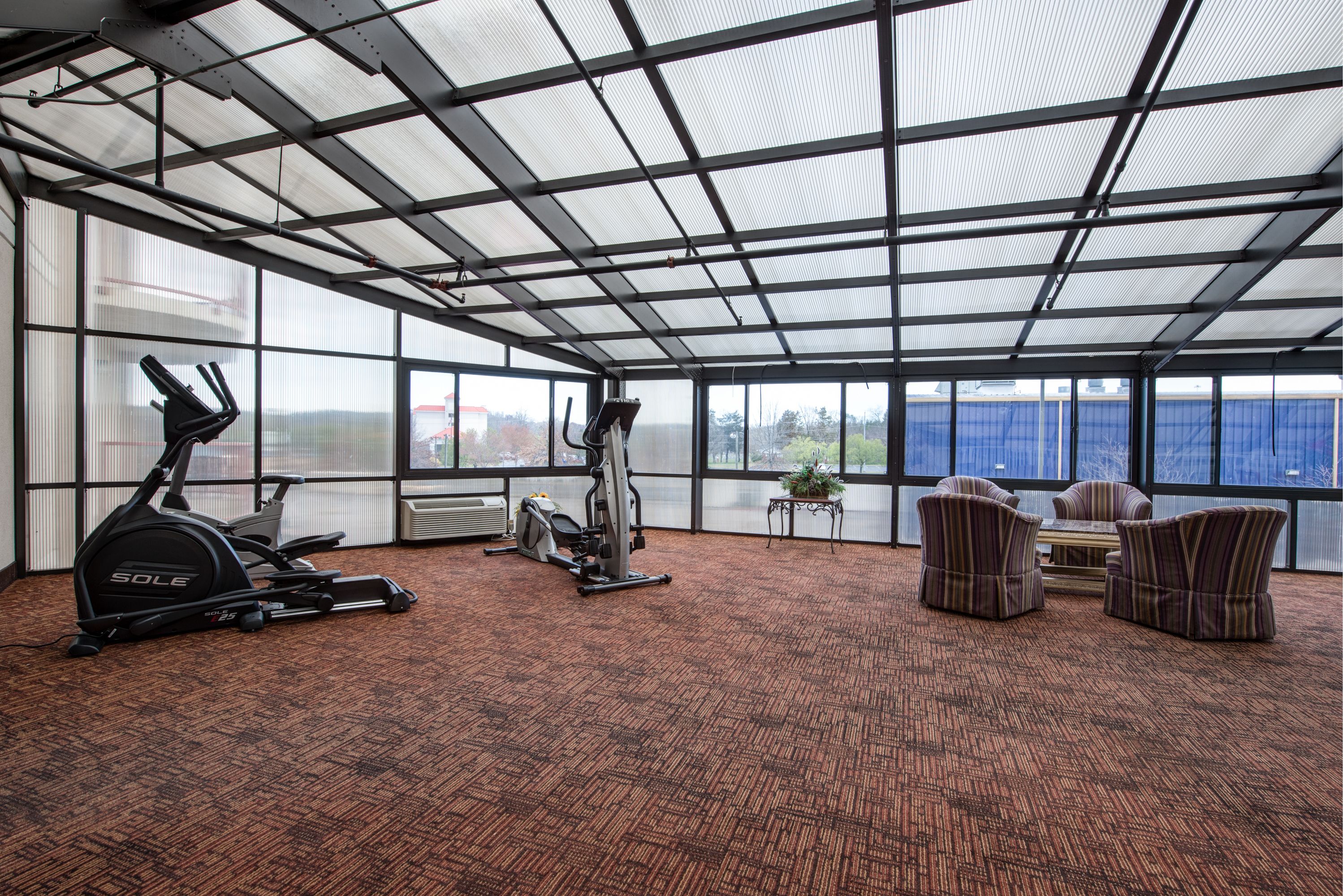 Une salle de sport équipée de matériel d’exercice, avec un espace détente, de grandes fenêtres et une vue sur l’extérieur.