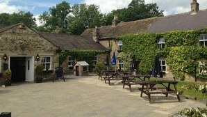 A stone building with ivy-covered walls and a paved courtyard with wooden picnic tables. - The Old Mill Knitsley (Consett)