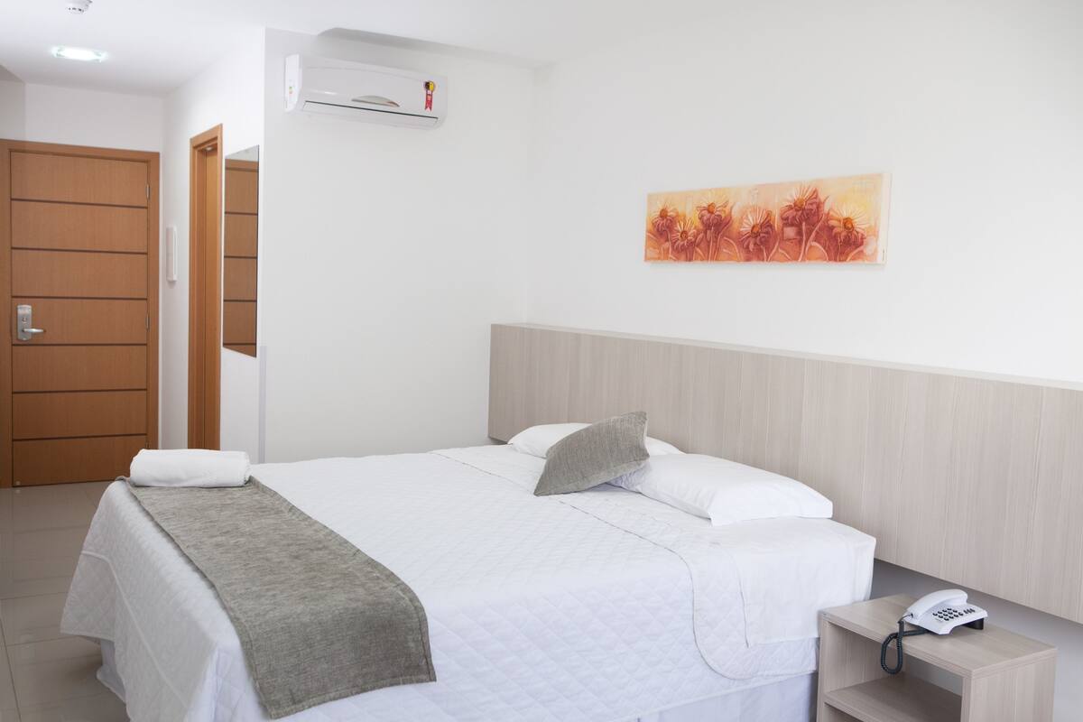 Ein Hotelzimmer mit einem Bett, einem Nachttisch mit Telefon, einem Bild an der Wand und einer Klimaanlage.