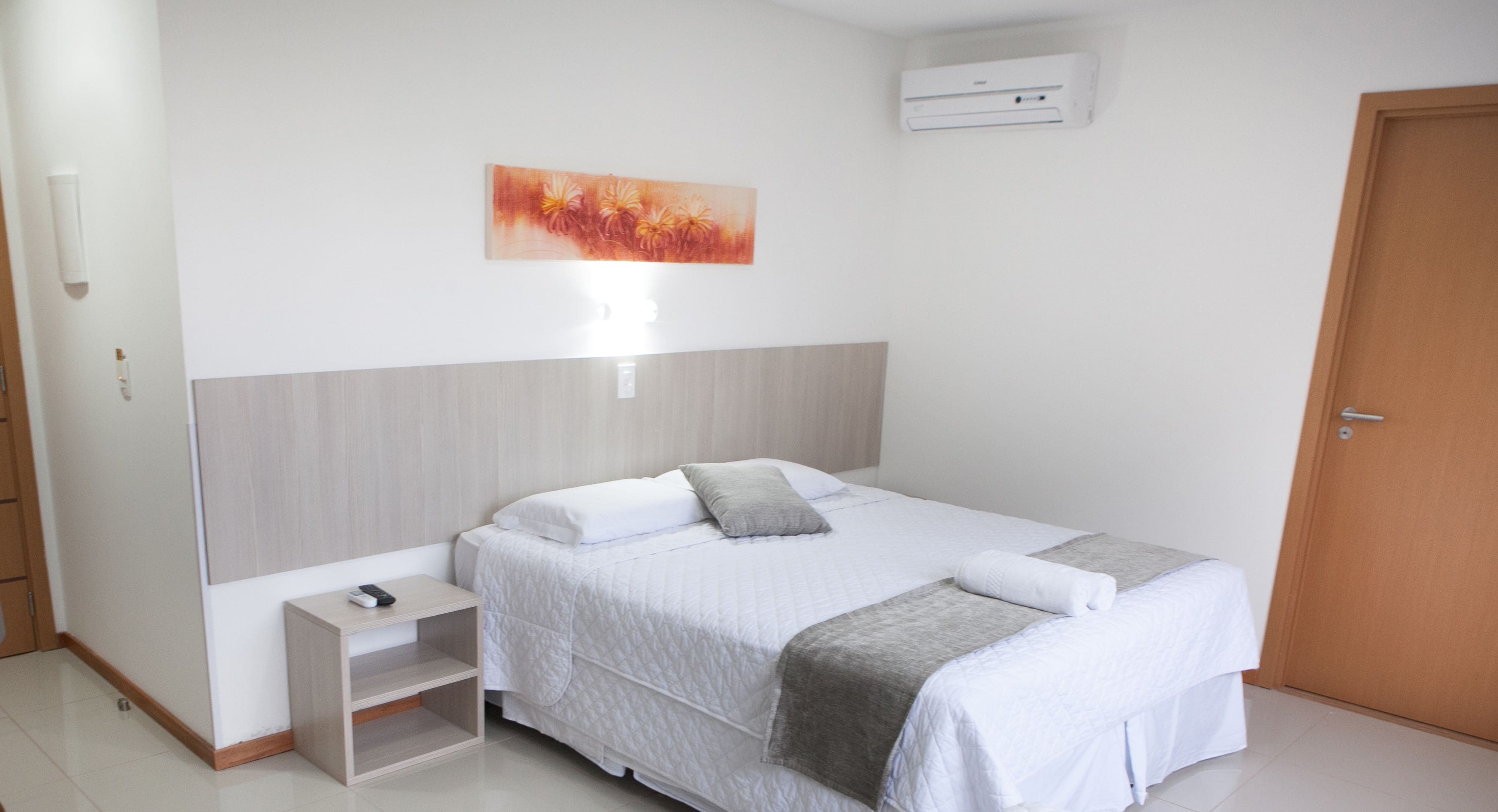 A bedroom with a bed, bedside table, and a wall-mounted air conditioner.