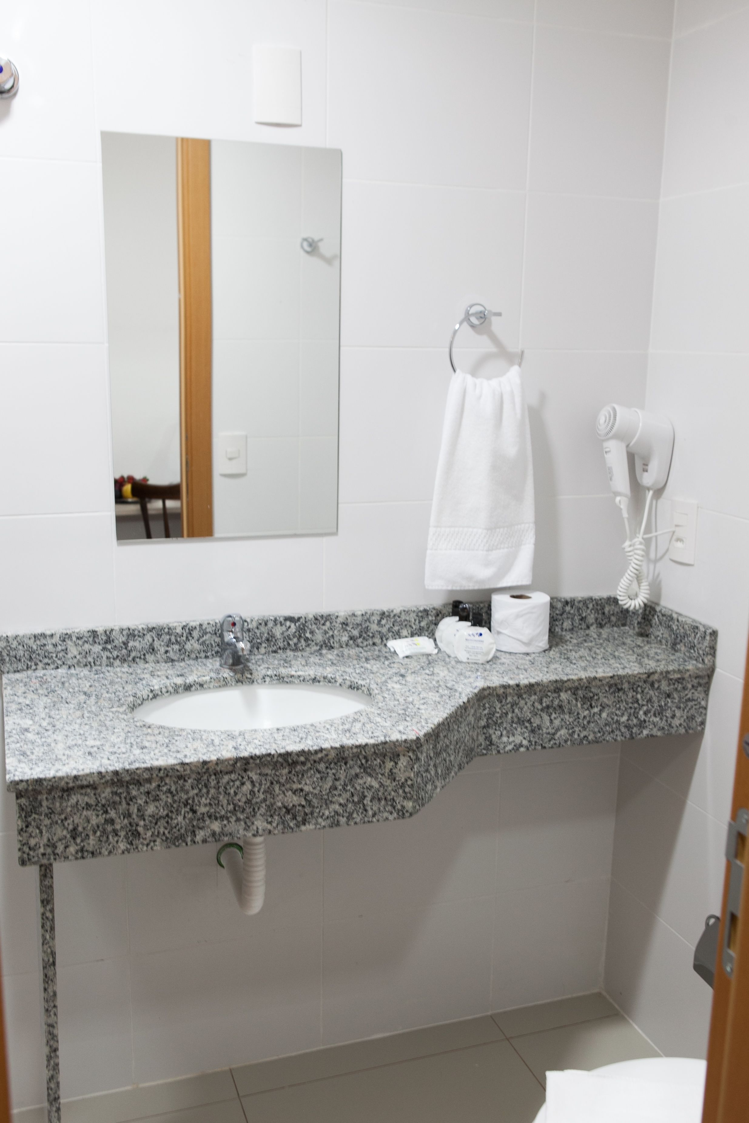 Et badeværelse med bordplade i granit, vask, spejl, håndklædestang, hårtørrer og toiletpapirholder.