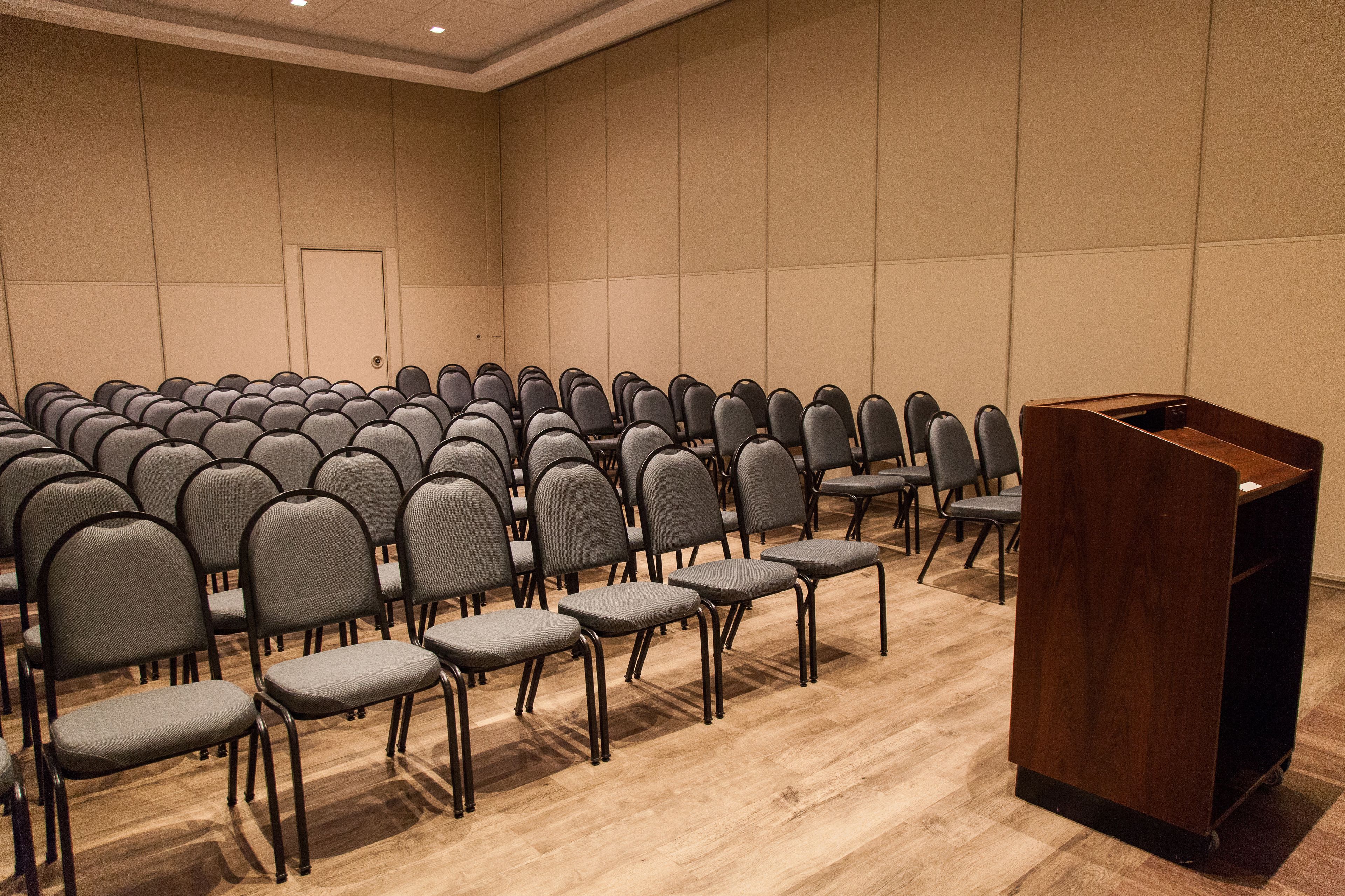 A conference room with rows of grey chairs and a wooden podium.