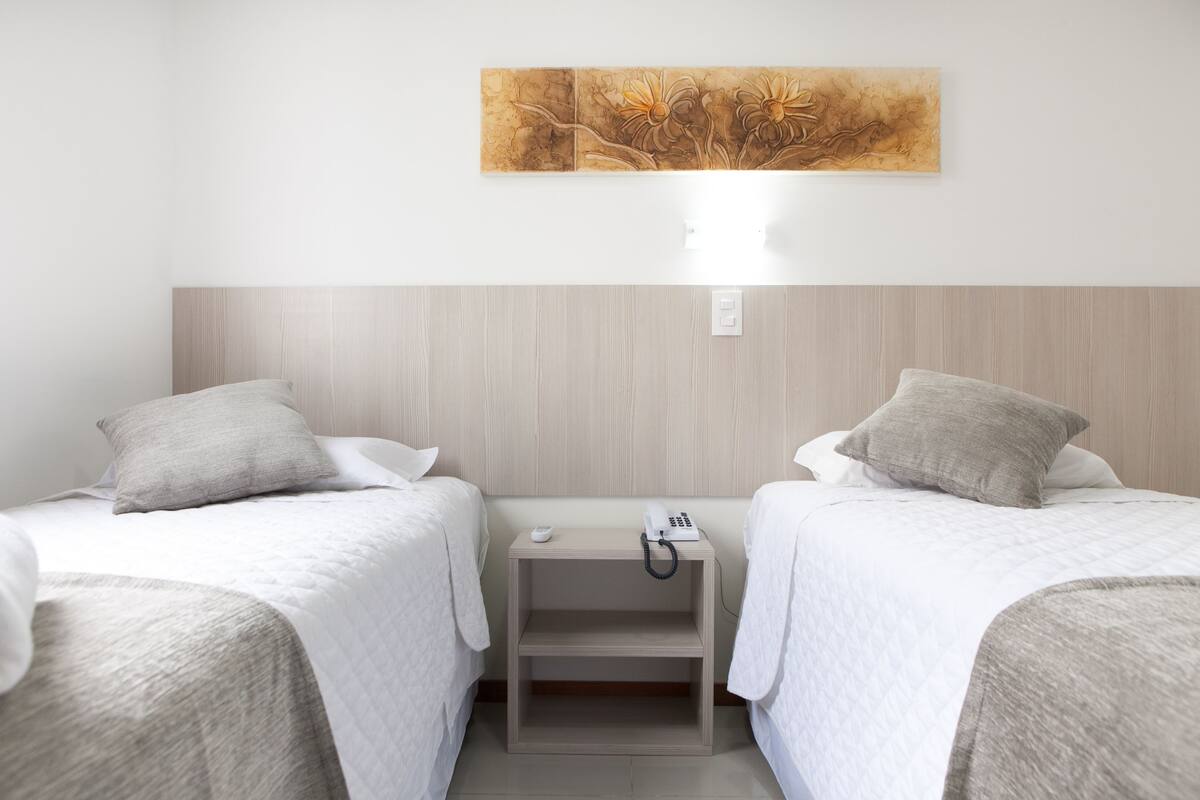 Ein Hotelzimmer mit zwei Betten, einem Nachttisch mit Telefon und einem an der Wand hängenden Kunstwerk.