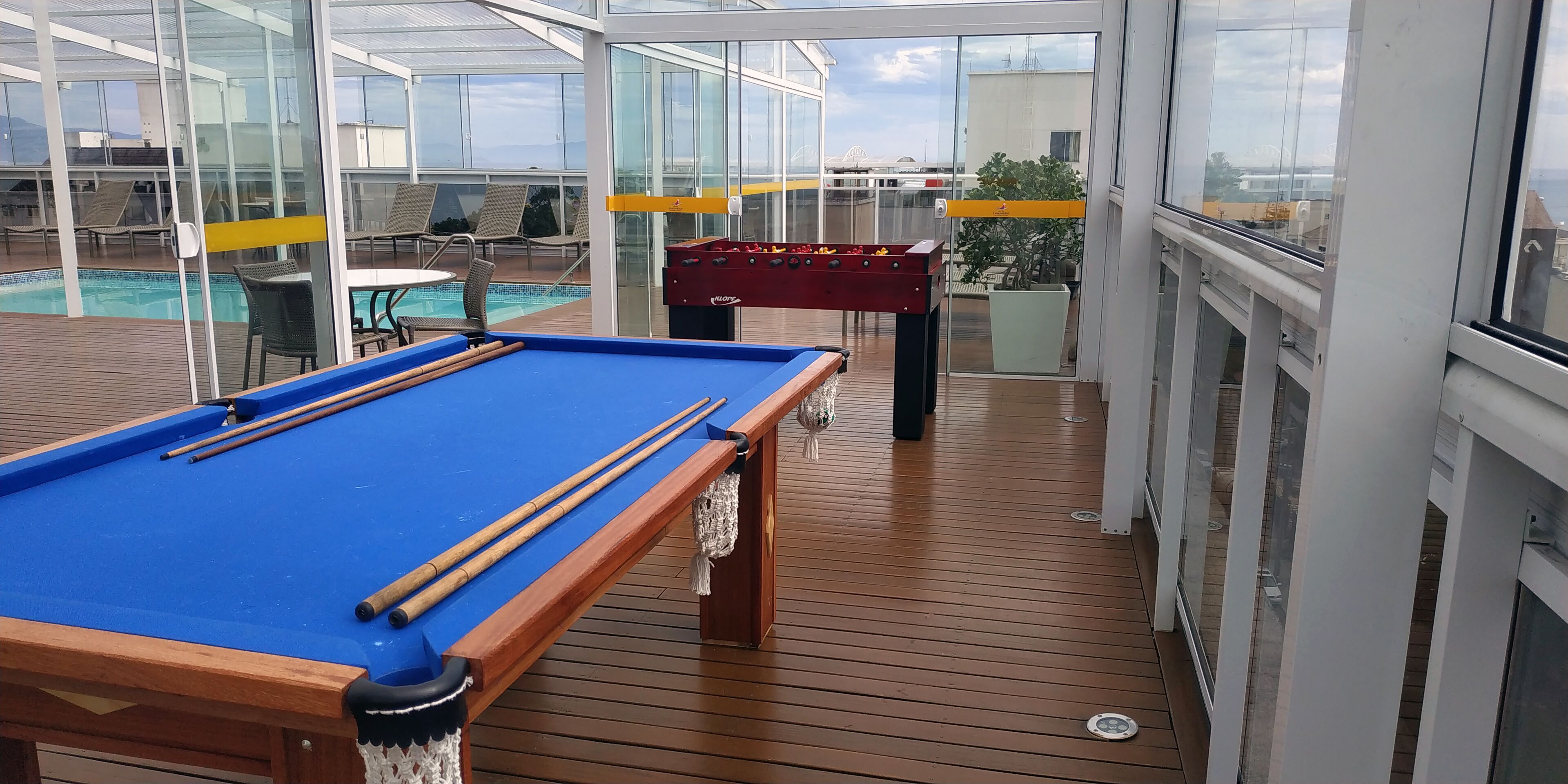 Un área de piscina con mesa de billar azul, mesa de futbolín roja y sillones de descanso.
