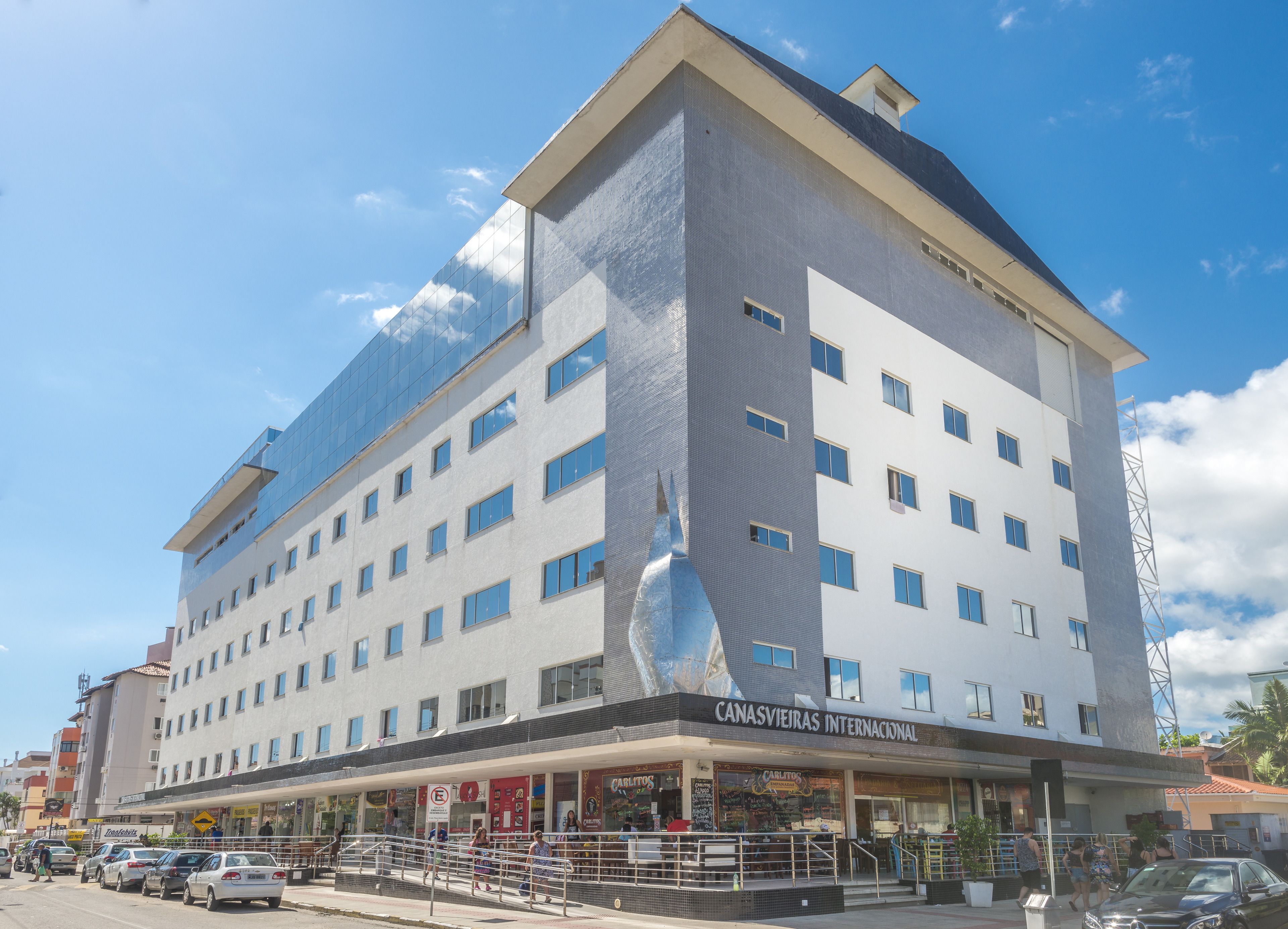 A multi-story hotel with a modern design, featuring a prominent glass facade and a sign for "Canasvieiras Internacional."