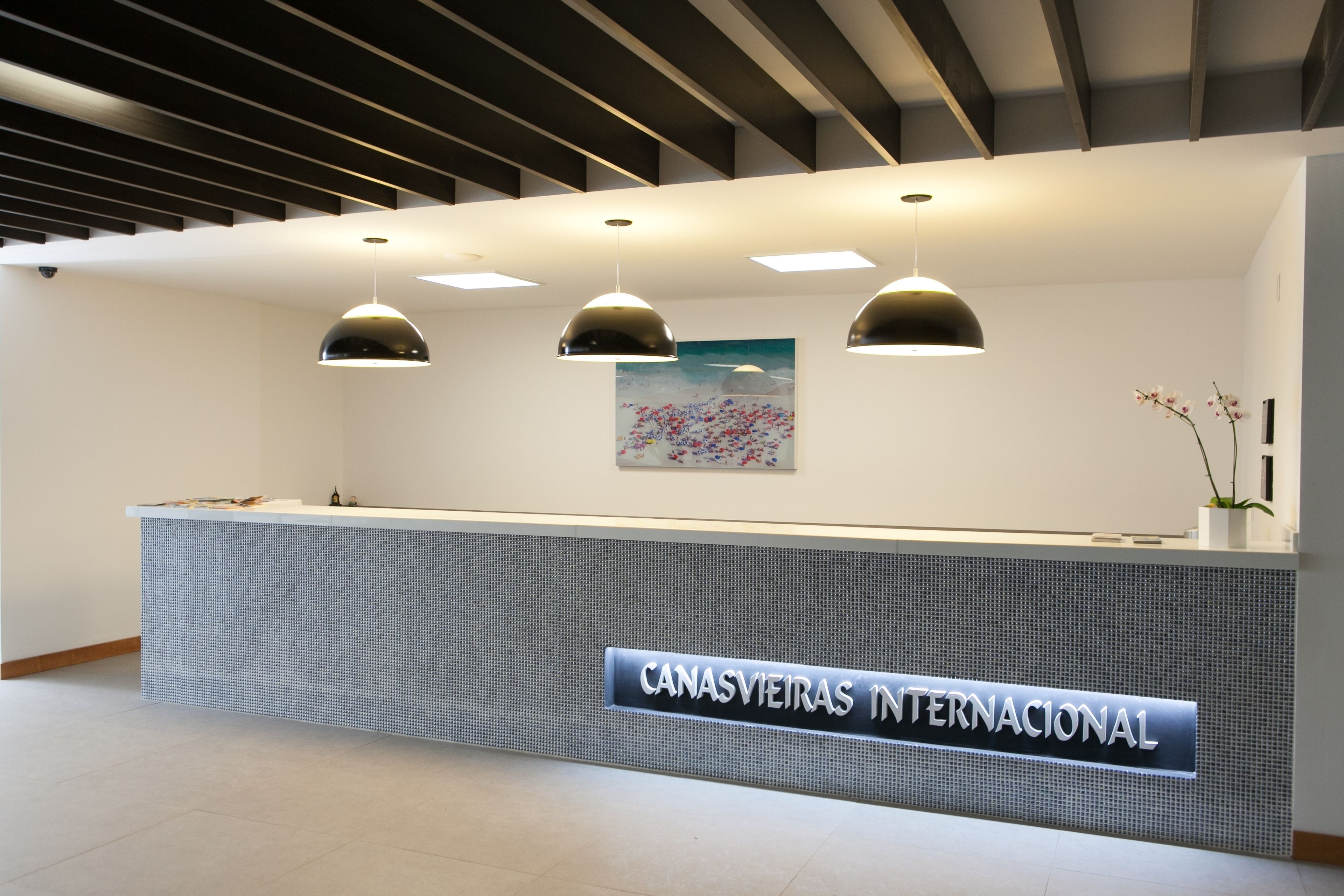 A reception desk with a sign reading "CANASVIEIRAS INTERNACIONAL" and three pendant lights above it.