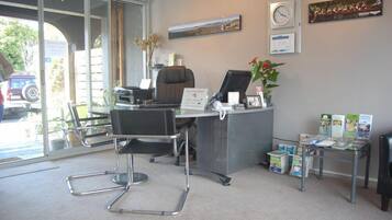 Un mostrador de recepción con una computadora, una silla, una planta y folletos informativos.