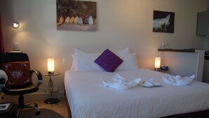A neatly made bed with white linens and a purple pillow, two bedside lamps, and a chair with a floral cushion. - Rotorua Motel (Rotorua)