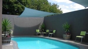 A swimming pool with a pebble-lined edge, surrounded by chairs and potted plants. - Rotorua Motel (Rotorua)