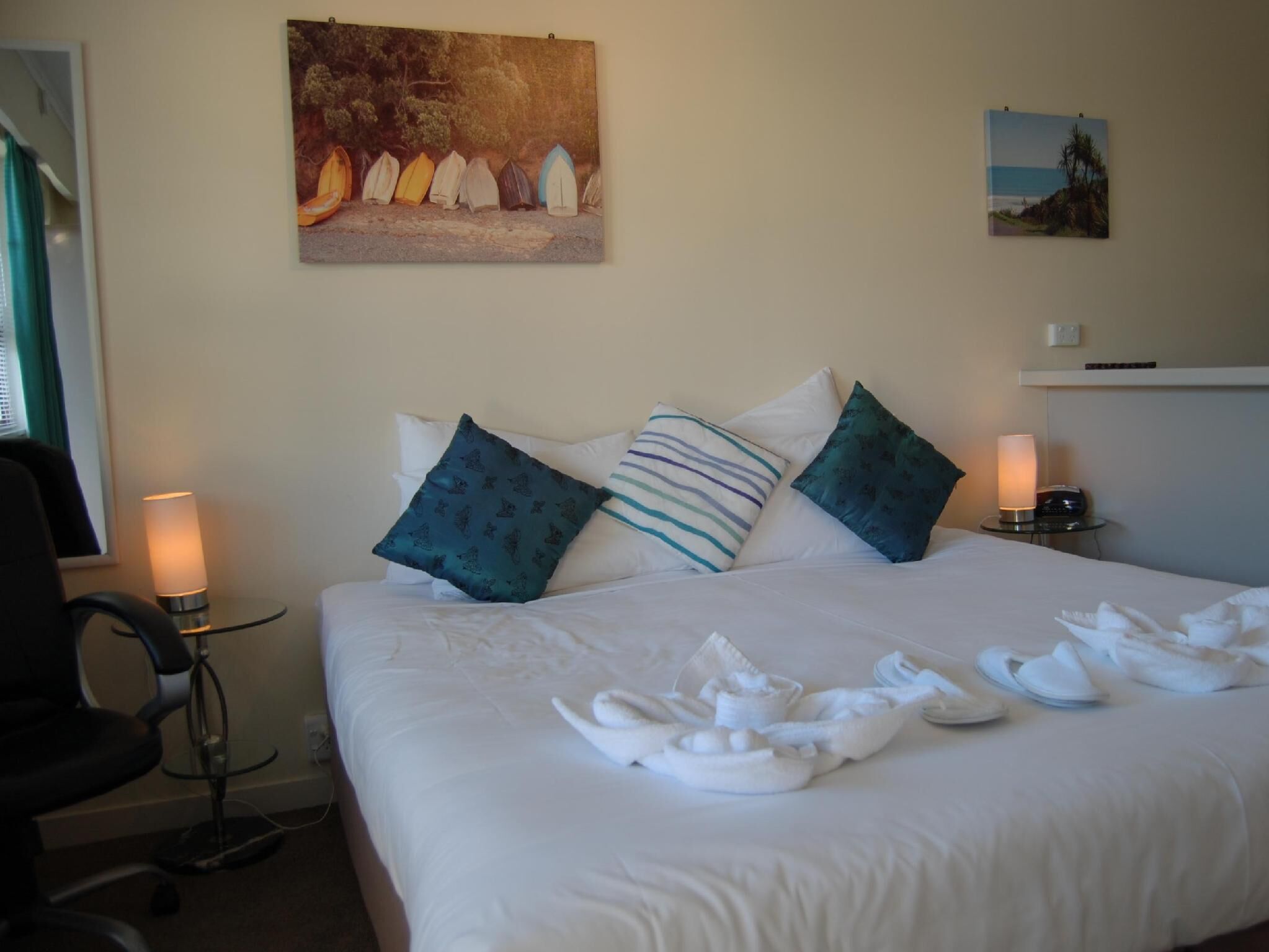 Ein Hotelzimmer mit Bett, Kissen, einem Gemälde, einem Schreibtisch mit Lampe und einem Sessel.