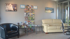 A room with a black leather chair, a beige sofa, and a glass coffee table with magazines and books. - Rotorua Motel (Rotorua)