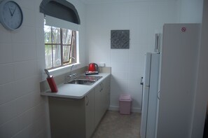 Eine kleine Küche mit Spüle, Wasserkocher, Kühlschrank und Mülleimer.