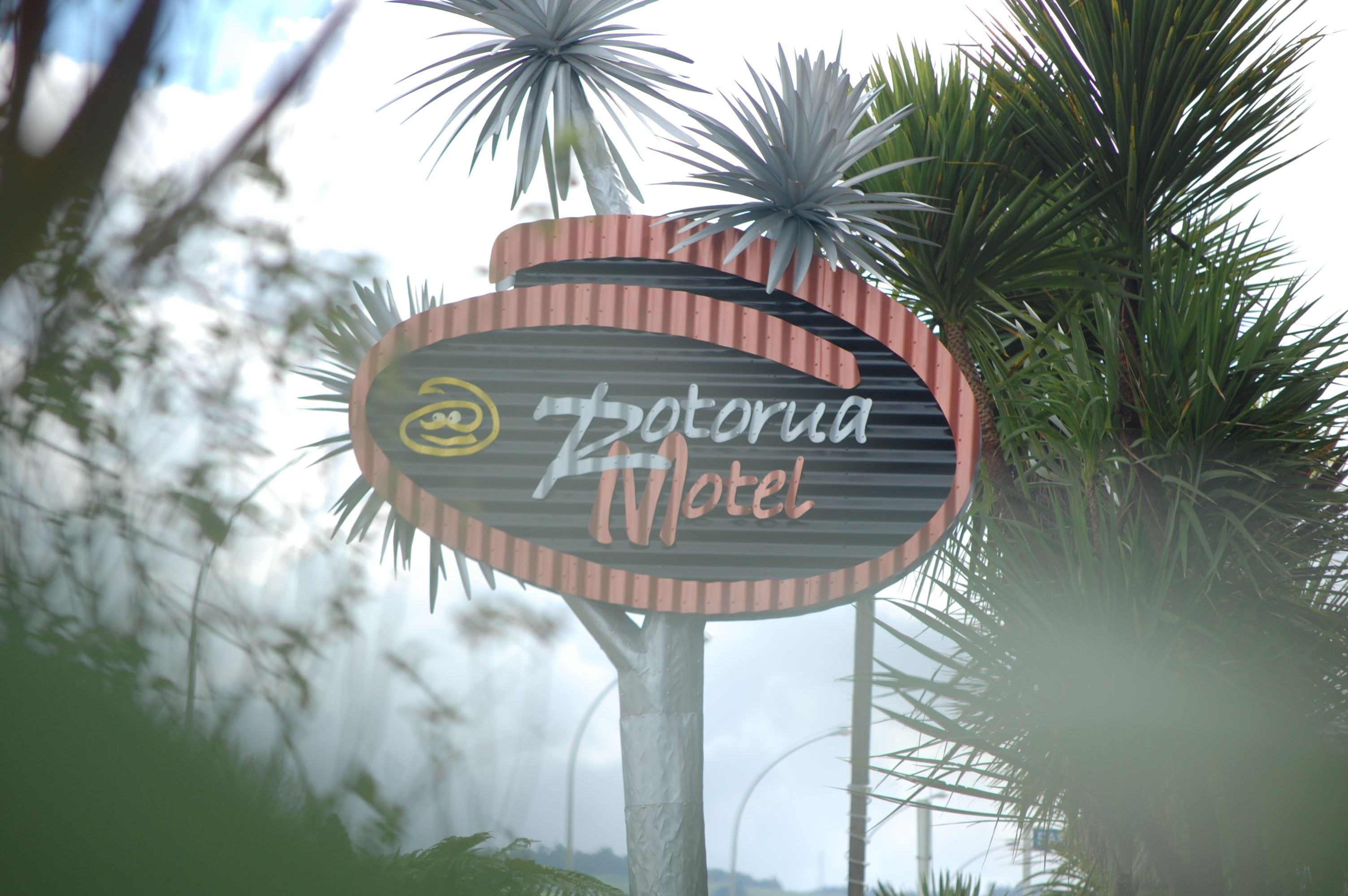 Une enseigne pour le «Zotoria Motel », avec un logo stylisé et du texte, le tout entouré de palmiers.