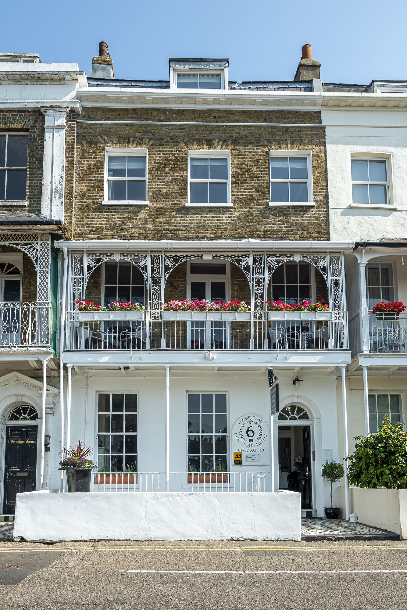 Un edificio de dos plantas con fachada blanca, múltiples ventanas y balcones con jardineras.