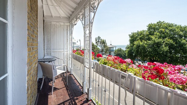 A balcony with a wicker chair, a metal railing, and a view of the sea.