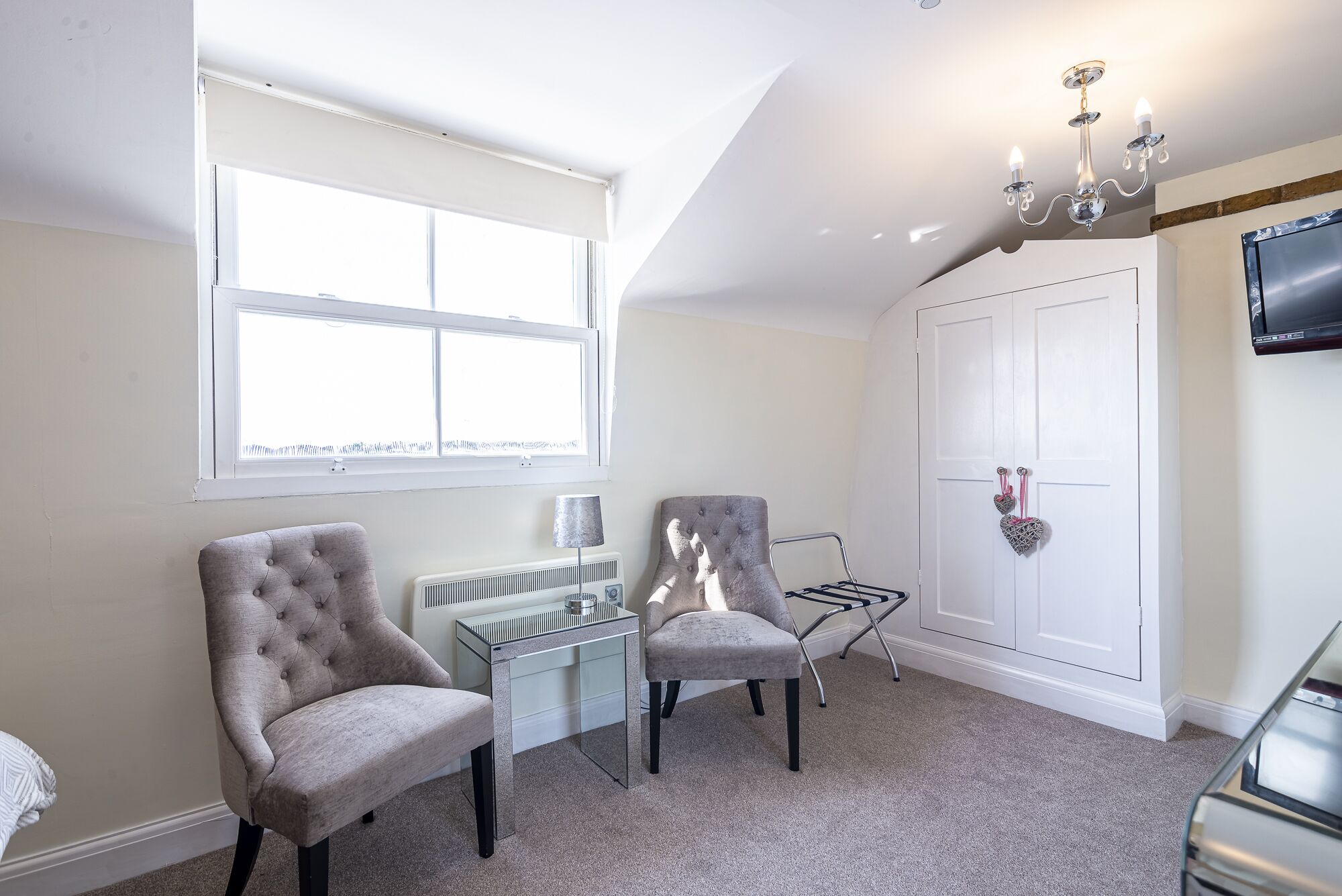 A room with two chairs, a radiator, a desk, a TV, and a wardrobe.