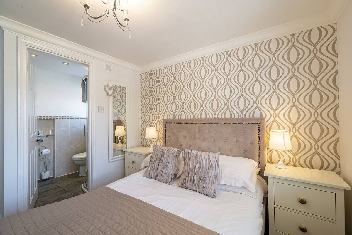 Een slaapkamer met een bed, nachtkastjes, een spiegel en een behang met patroon.