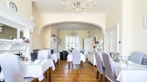 A formal dining room with white tables and chairs, a chandelier, and a fireplace.