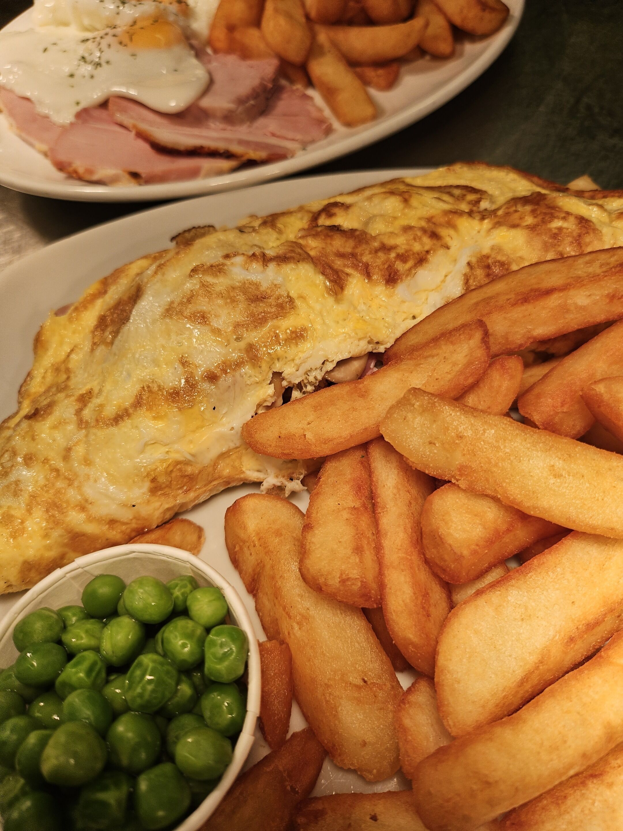 A plate with a fried egg, fries, and peas.