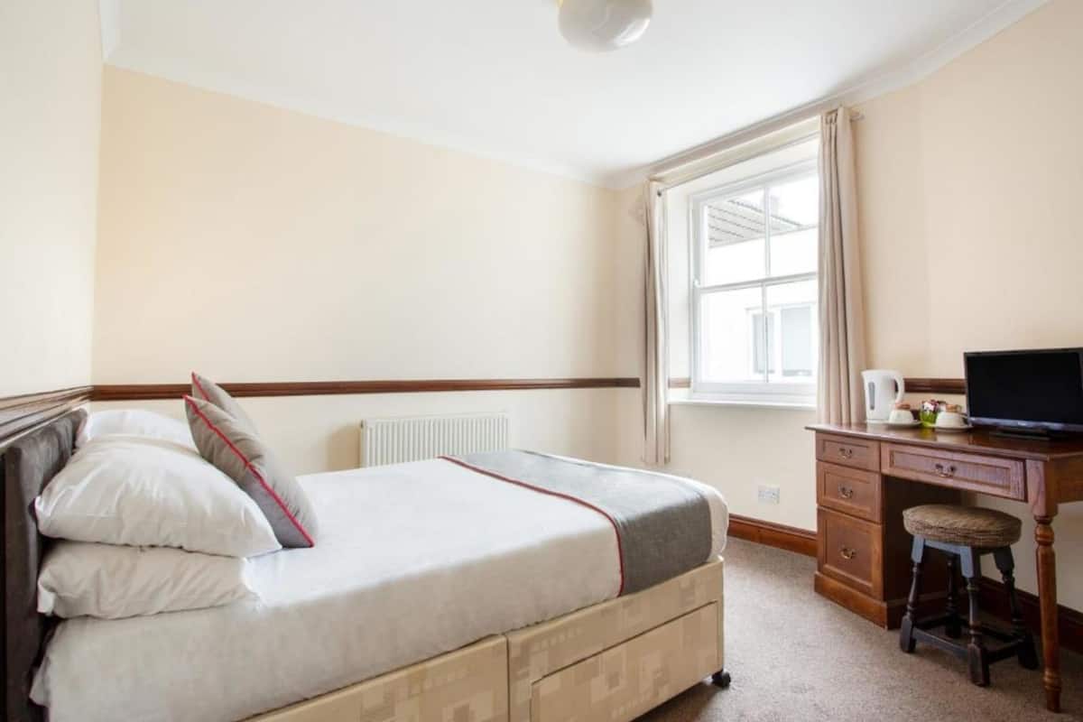 A bedroom with a bed, a desk, a chair, a radiator, and a window.