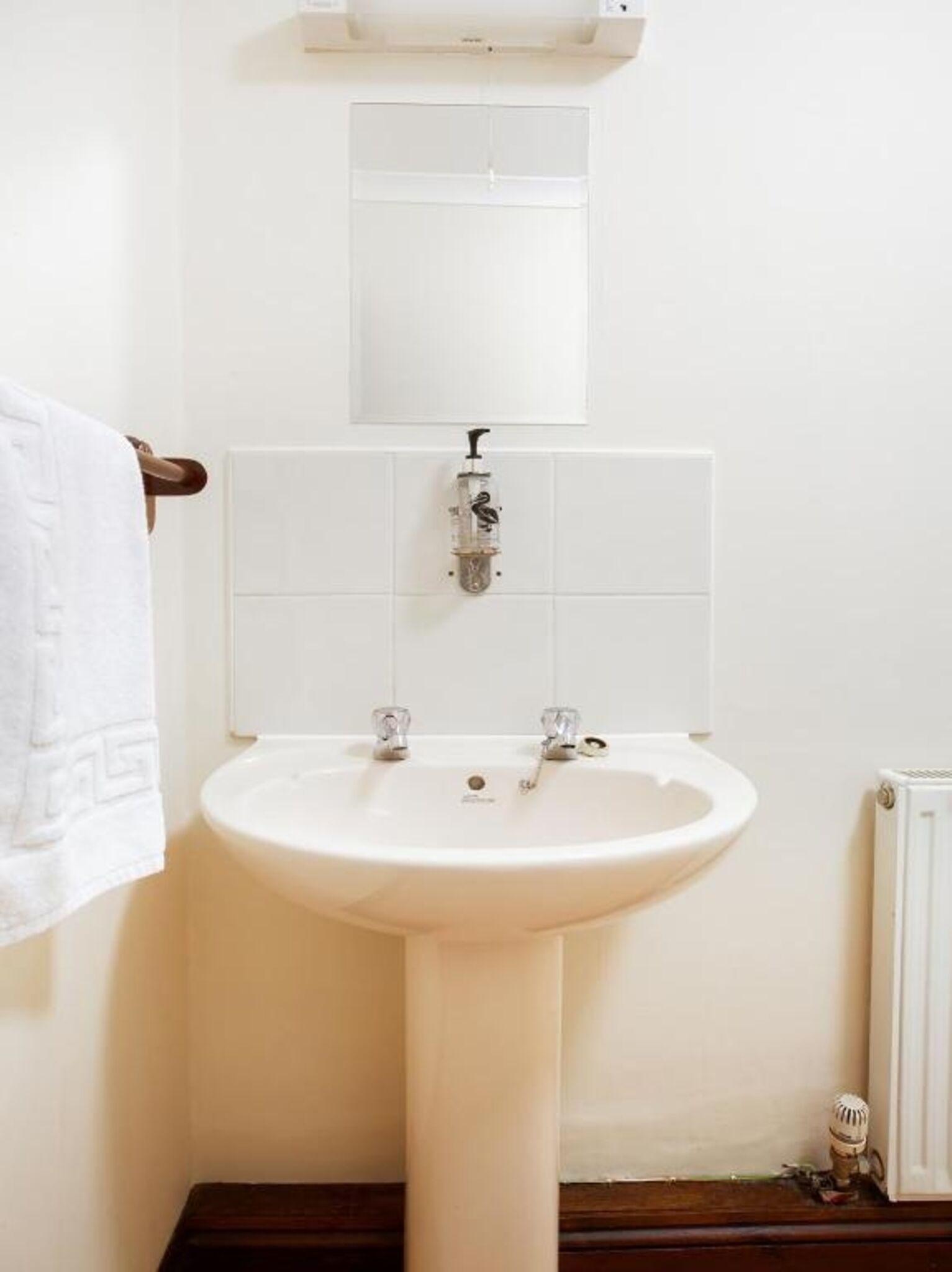 Un baño con un lavabo blanco, dos grifos y un espejo sobre el lavabo.