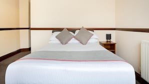 Een hotelkamer met een bed, kussens, een nachtkastje en een radiator.