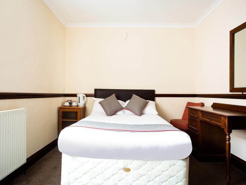 A hotel room with a bed, a nightstand, a desk, and a mirror.