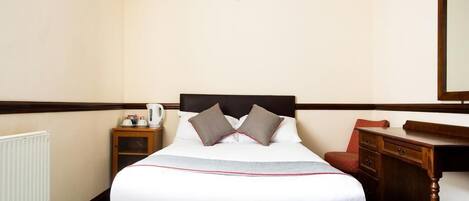 A hotel room with a bed, a nightstand, a desk, and a mirror.