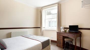 A bedroom with a bed, a desk with a computer, a radiator, and a window with curtains.