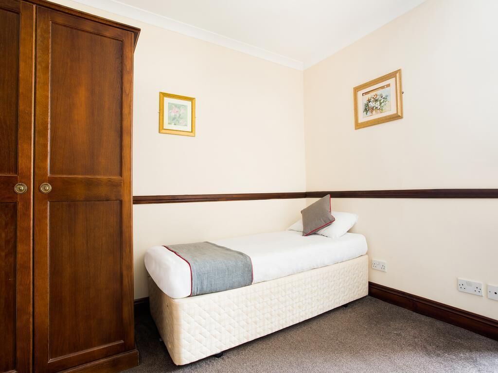 Un dormitorio con un armario de madera, una cama individual y dos cuadros en la pared.