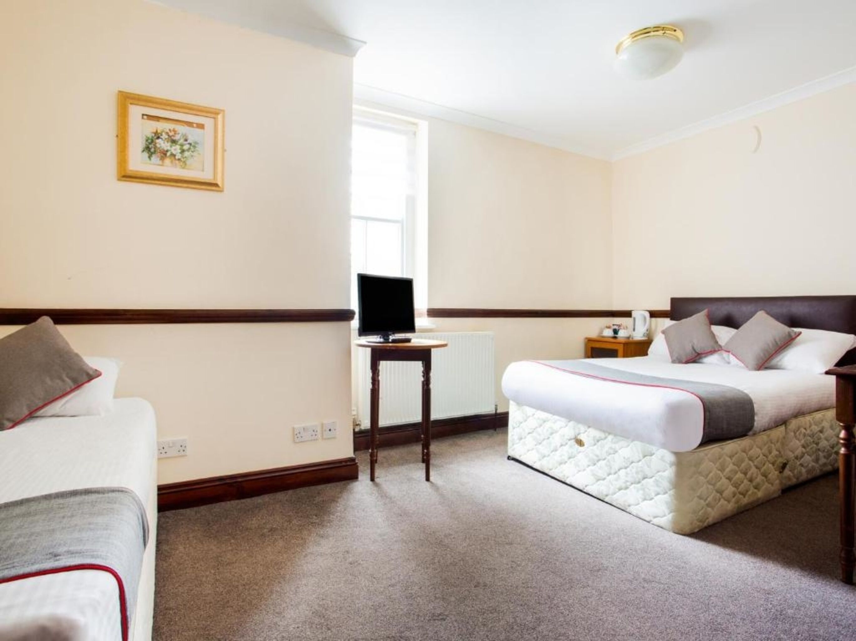 A hotel room with a bed, a desk with a computer, a small table, and a window.