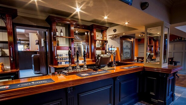 Een bar met een houten toonbank, meerdere tappunten en een spiegel die de ruimte weerspiegelt.