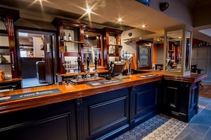 A bar area with a wooden counter, multiple taps, and a mirror reflecting the room.