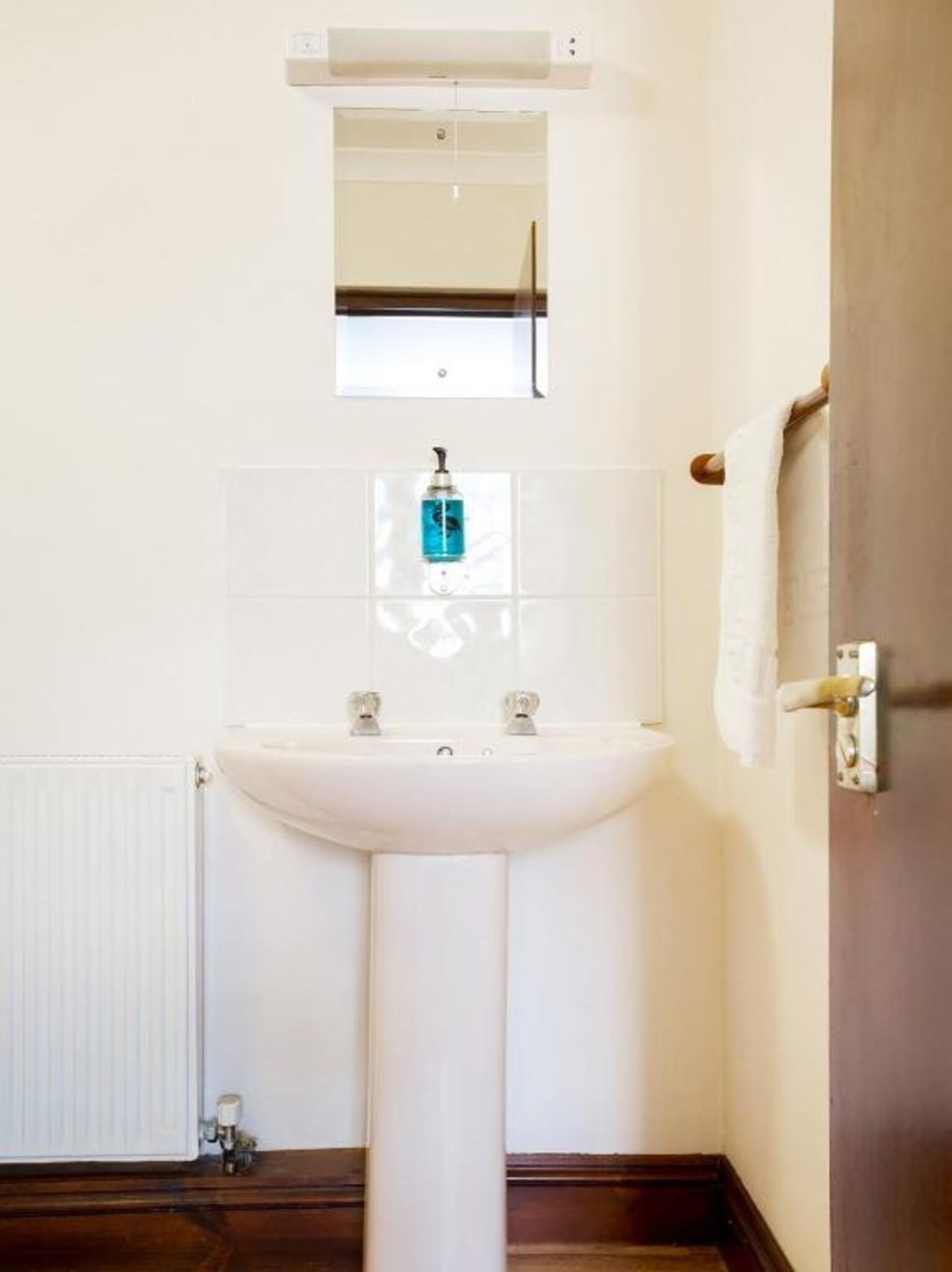 A bathroom with a white sink, a mirror above it, and a towel hanging on a door.