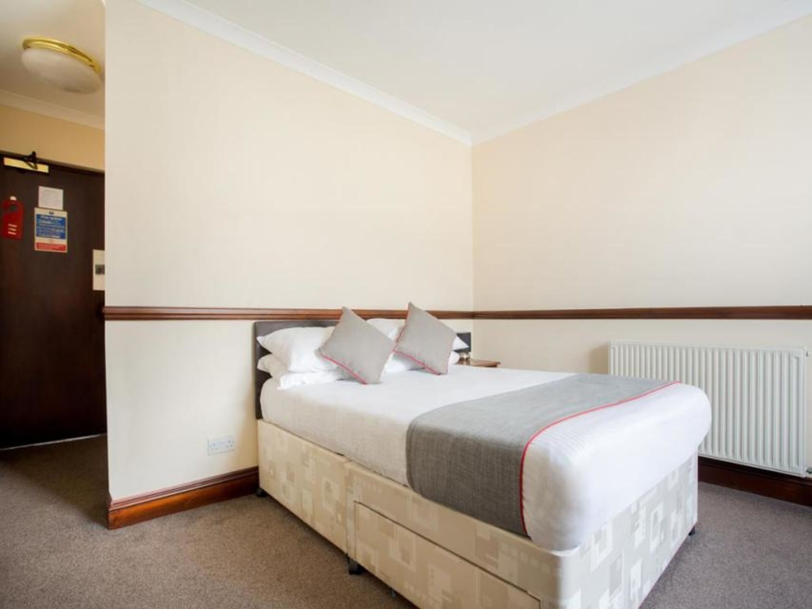 A hotel room with a bed, a radiator, and a door with a sign.