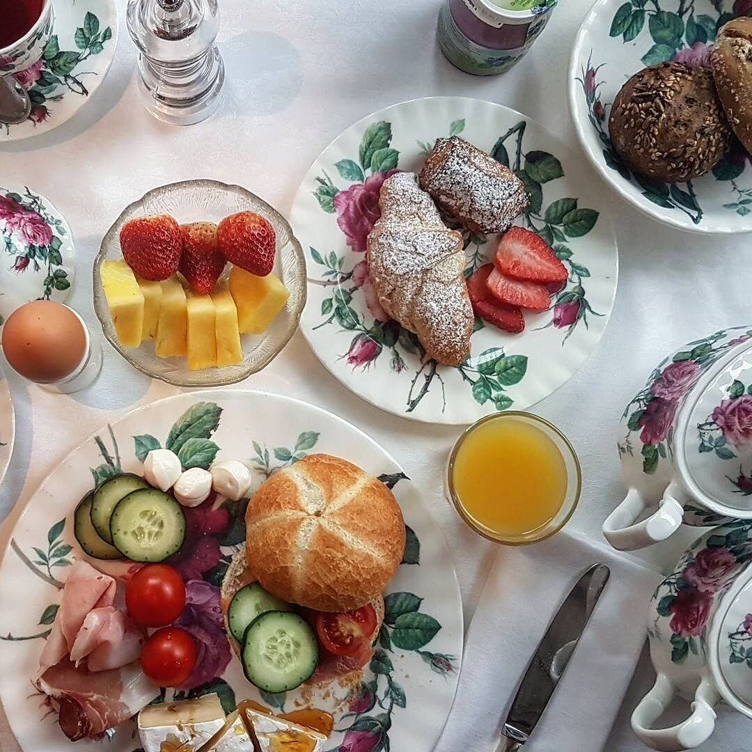 A breakfast table with plates of food, a jug of orange juice, and a teapot.