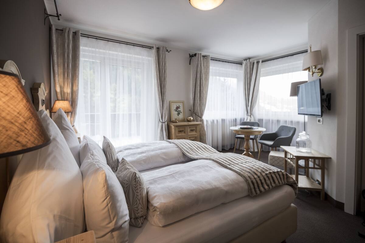 A hotel room with a double bed, a desk, a chair, a lamp, and a television.