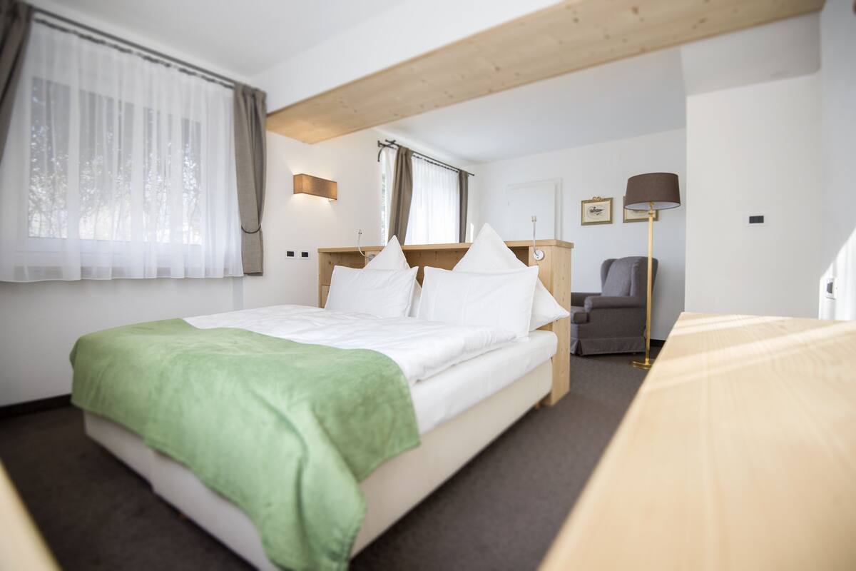 A hotel room with a bed, a desk, a chair, a lamp, and a window with curtains.