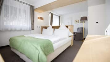 A hotel room with a bed, a desk, a chair, a lamp, and a window with curtains.
