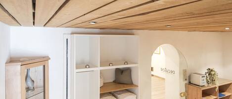 Techo de madera con armario empotrado y estanterías, una puerta blanca y una pequeña escalera que conduce a otra habitación.