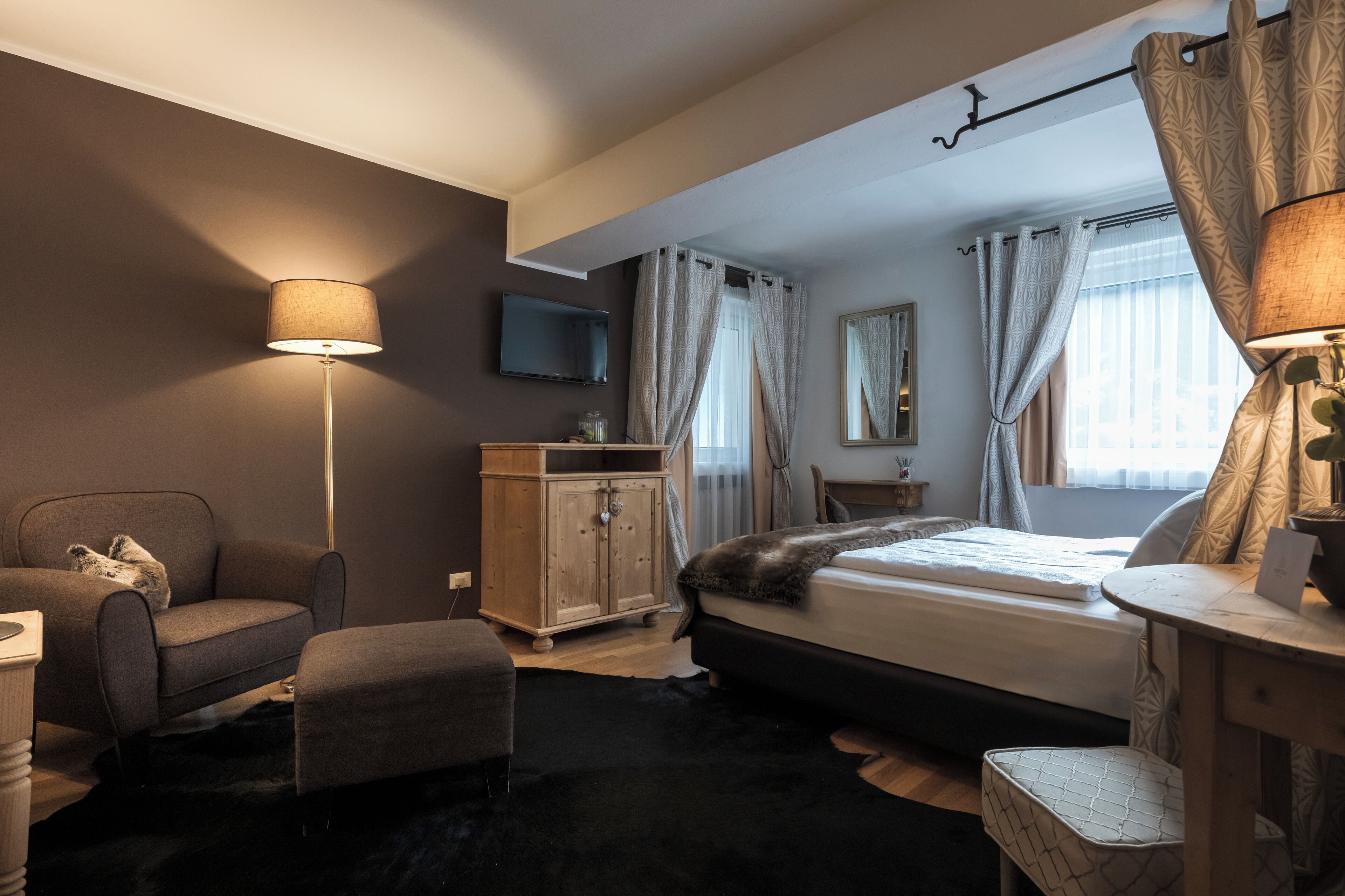 A bedroom with a bed, a chair, a desk, a TV, and a wardrobe.