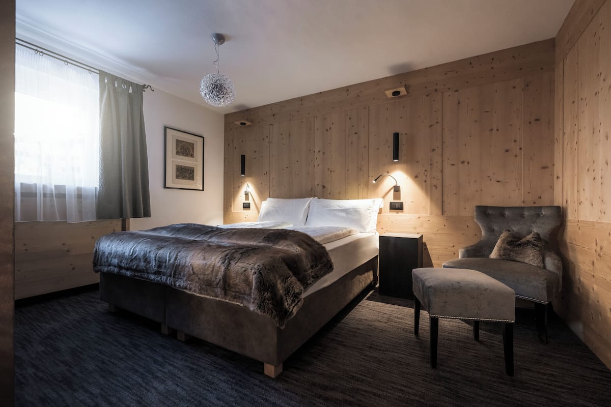 A bedroom with a large bed, a chair, and two wall-mounted lamps.
