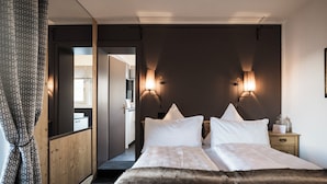 A hotel room with a double bed, wooden wardrobe, two bedside lamps, and a mirror.