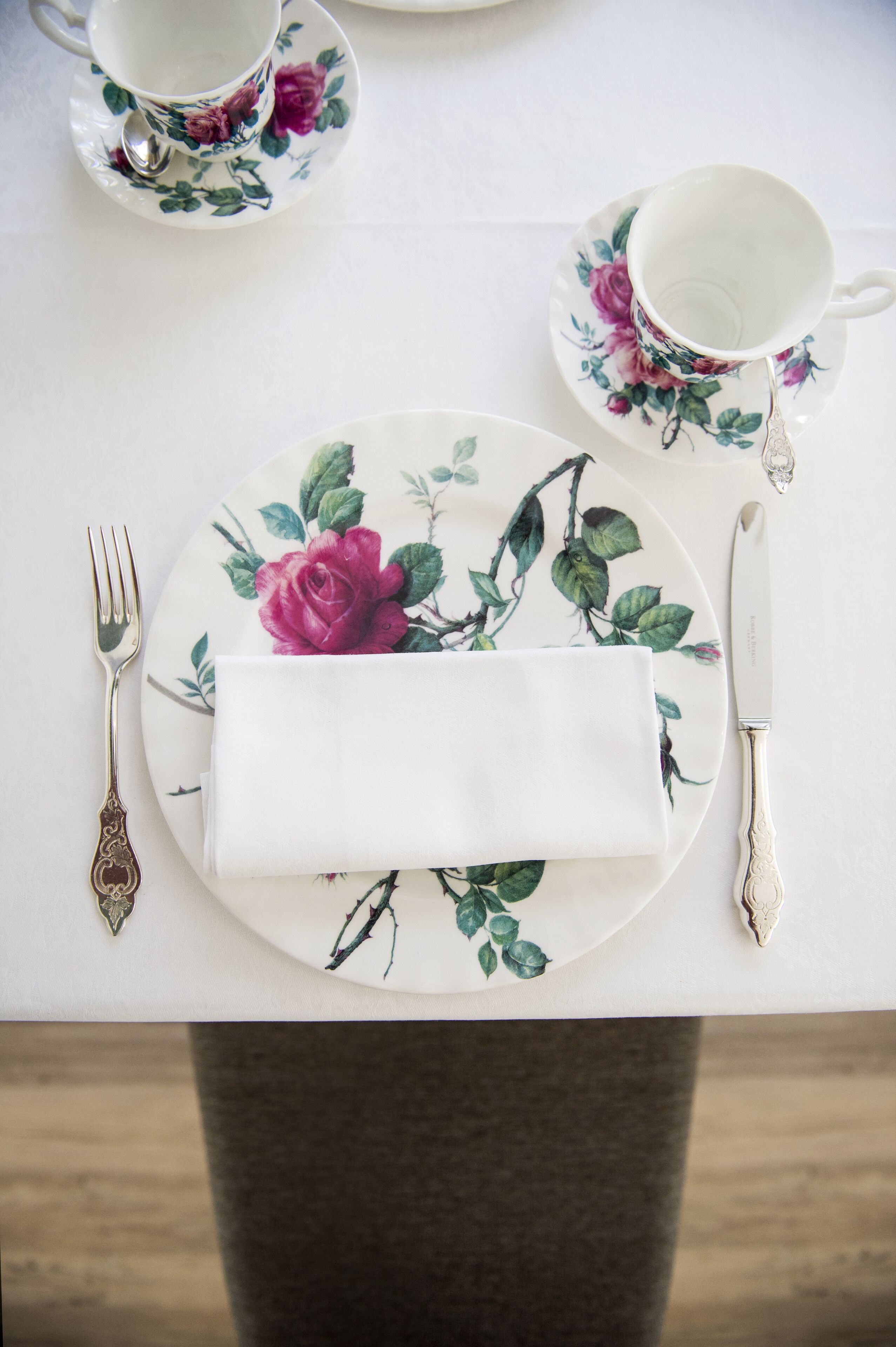 A table set with a floral plate, a folded napkin, a fork, a knife, and a cup.