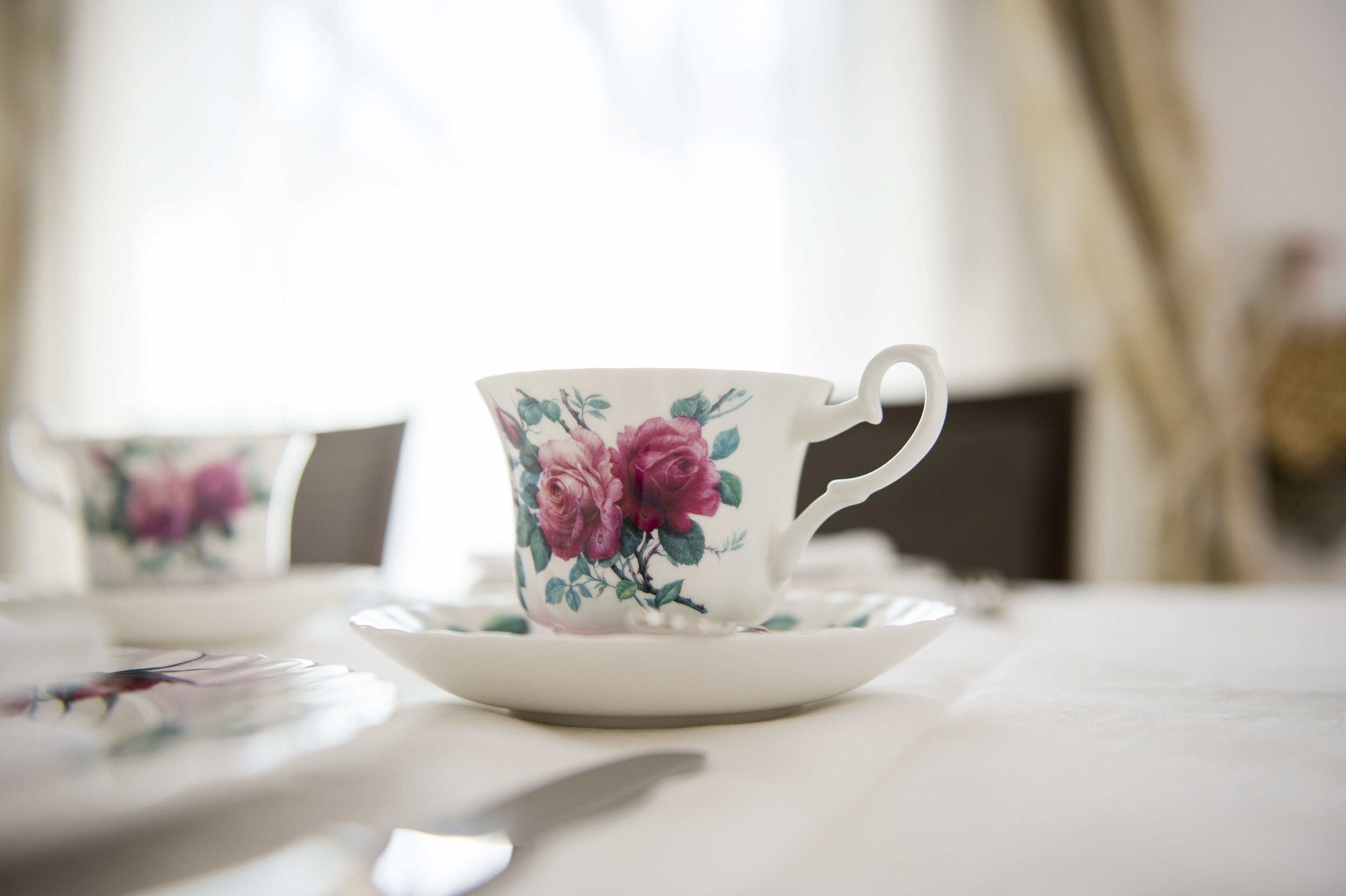 A white table with a floral-patterned cup and saucer, a knife, and a blurred background.