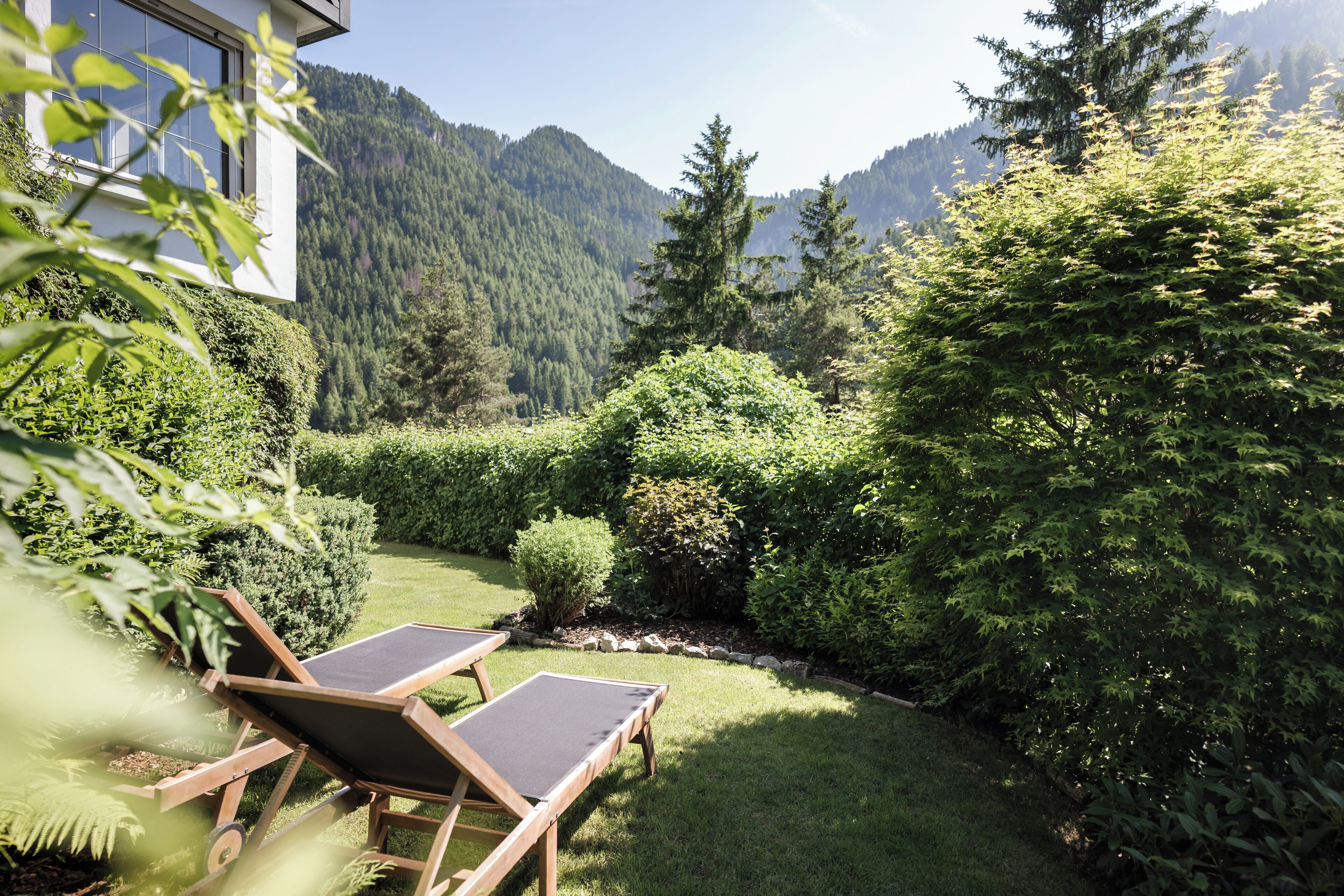 A garden with two wooden lounge chairs, a well-maintained lawn, and a mountain backdrop.